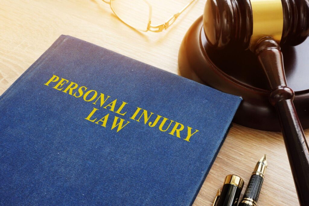 Blue Personal Injury Law book rests on desks near gavel, two fancy pens and pair of glasses