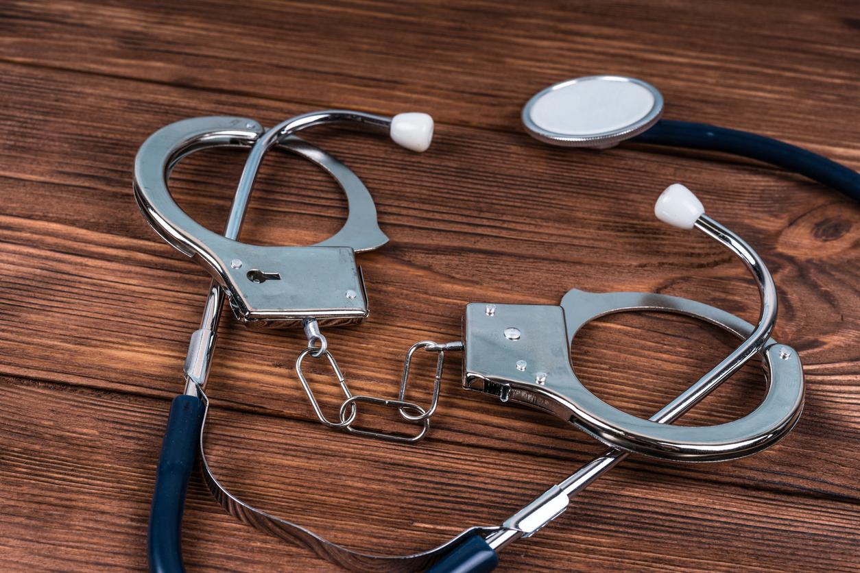 Metal handcuffs are hooked around a stethoscope lying on top of a brown desk