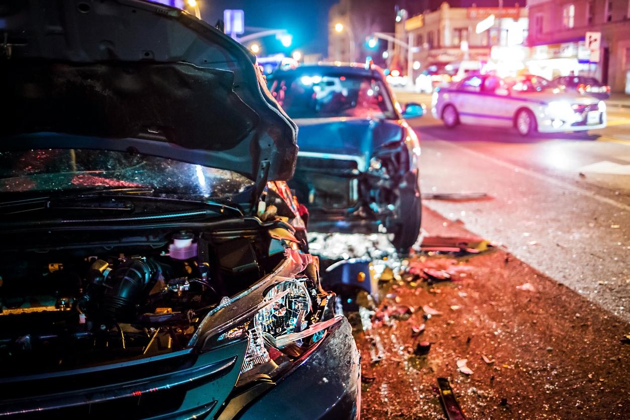 Night time photo of car accident showing broken glass on ground and smashed bumpers