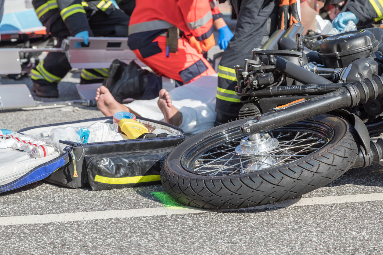 Paramedics help motorcycle rider after crash, readying him on the stretcher.