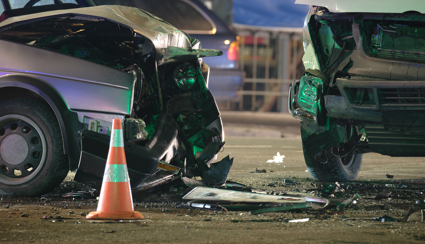 Damaged in heavy car accident vehicles after collision on city street crash site at night.