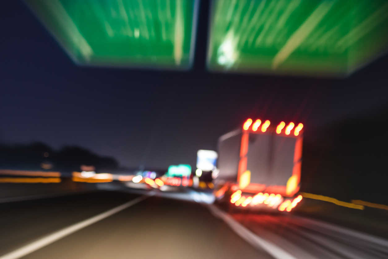 Defocused blurred motion of semi truck speeding on highway under street signs